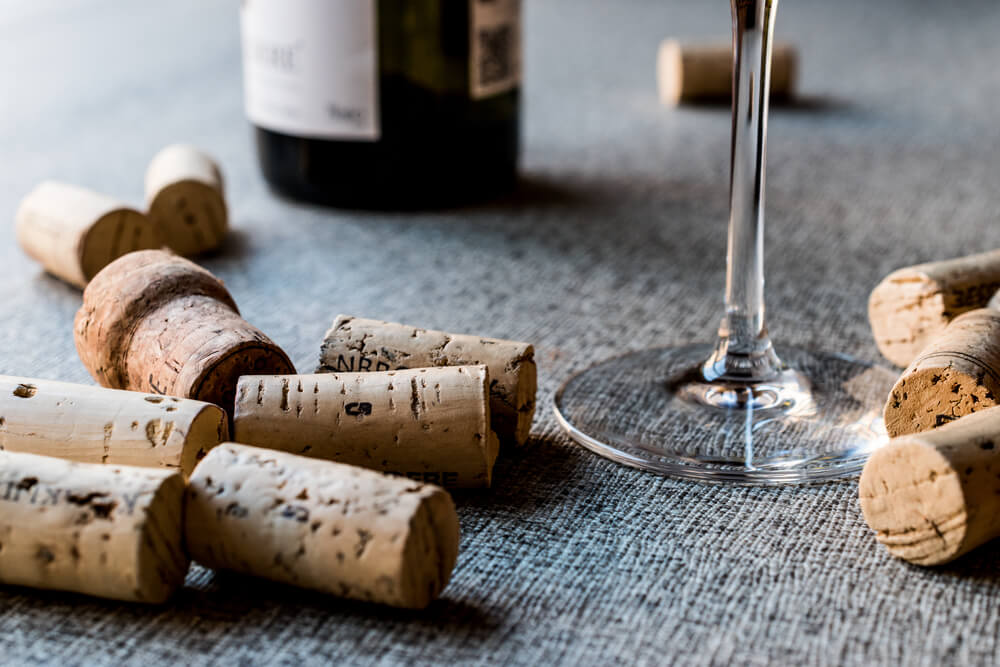 Imagem de várias rolhas de vinho soltas em uma mesa ao lado de uma garrafa e uma taça.