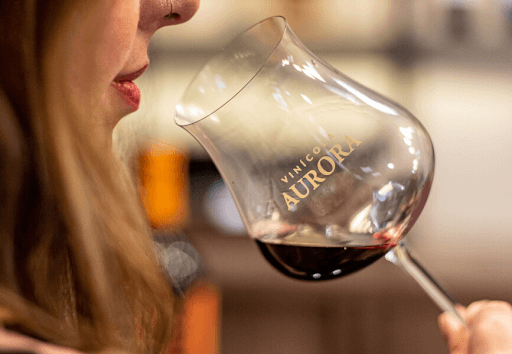 Imagem de uma mulher tomando vinho em uma taça da vinícola Aurora