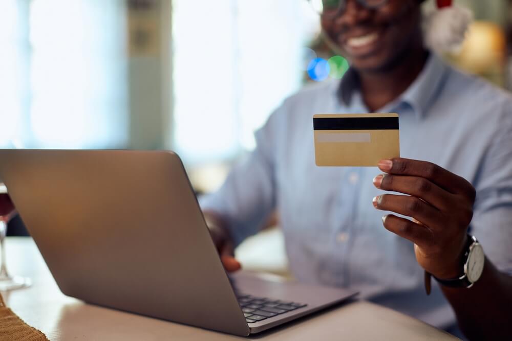 Homem Negro Escolhendo Vinho No Computador, Segurando Um Cartão De Crédito, Na Black Friday.