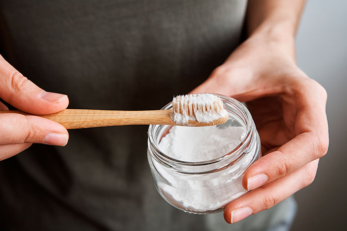 pessoa segurando uma escova de dente e um pote de bicarbonato