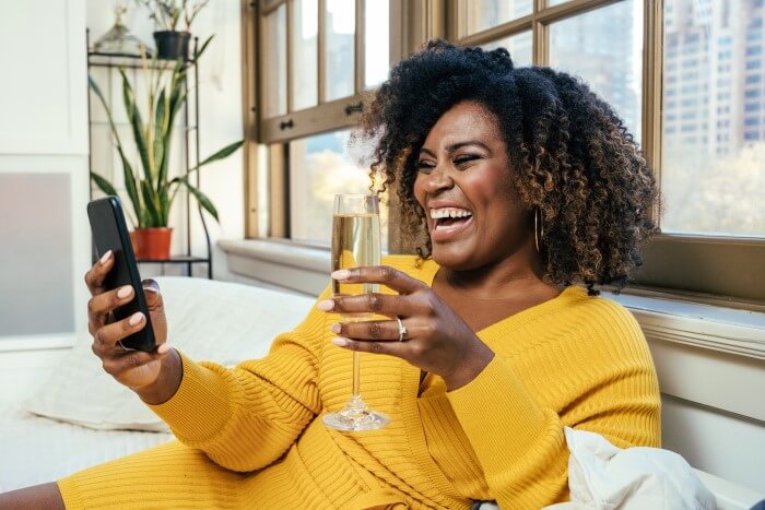 mulher usando o telefone e tomando uma taça de espumante