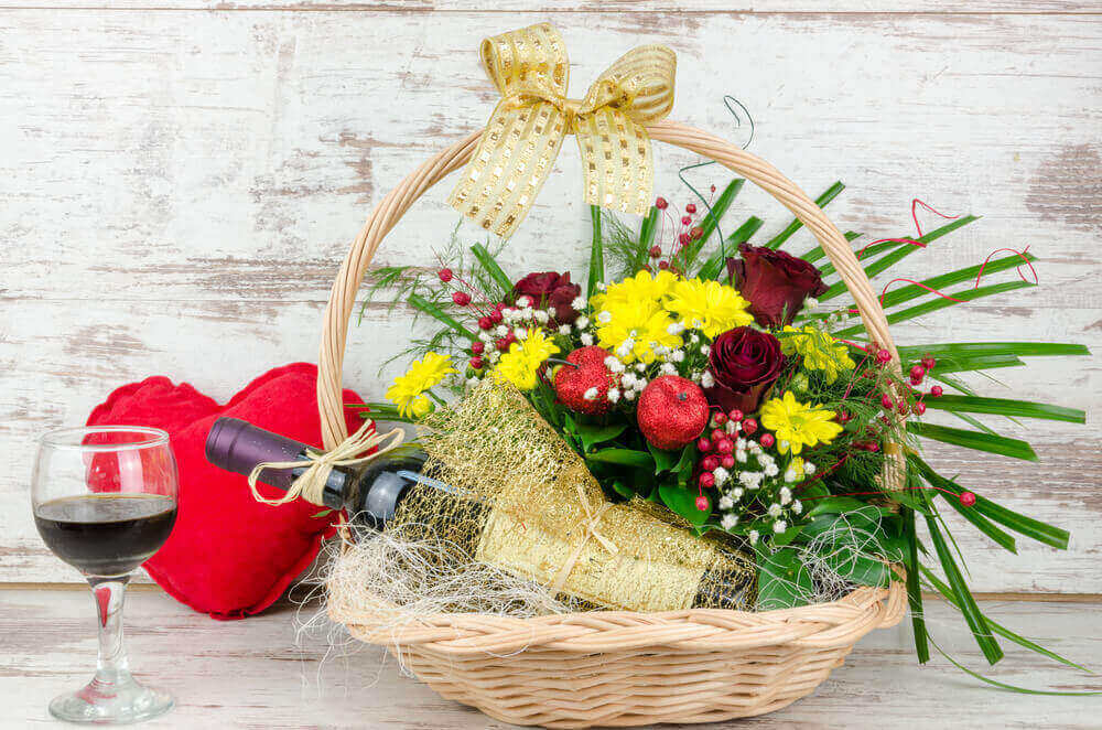 Imagem de uma cesta decorada com flores e uma garrafa de vinho dentro.