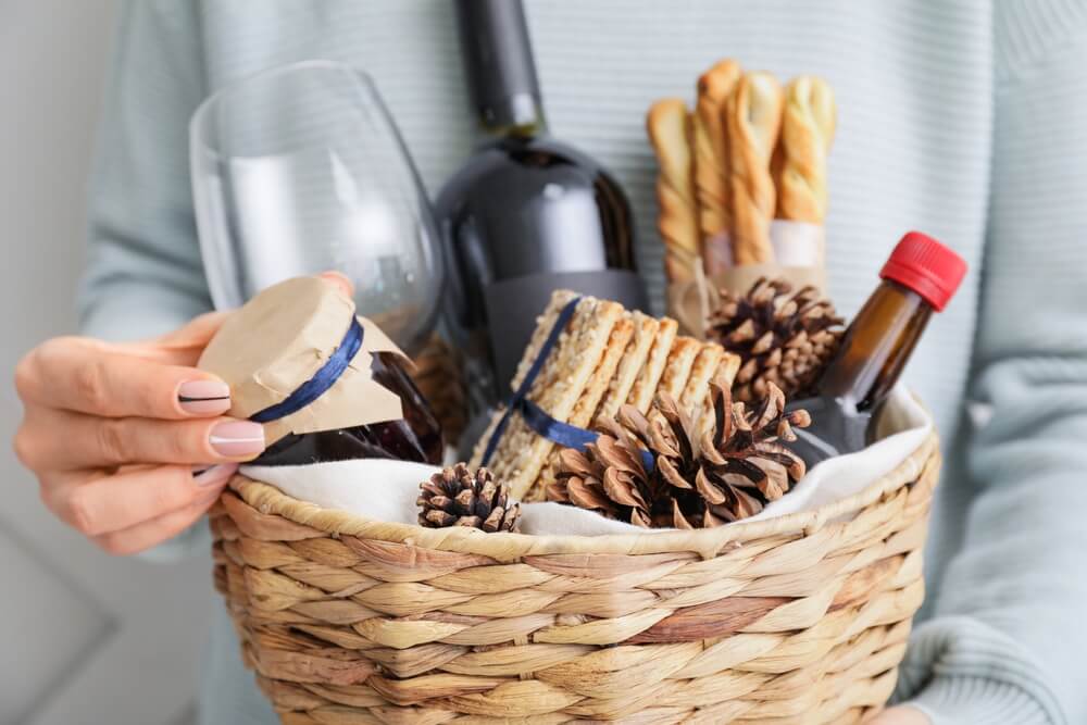 Uma Pessoa Segura Uma Cesta Com Vinho E Produtos Gourmet, Além De Uma Taça.