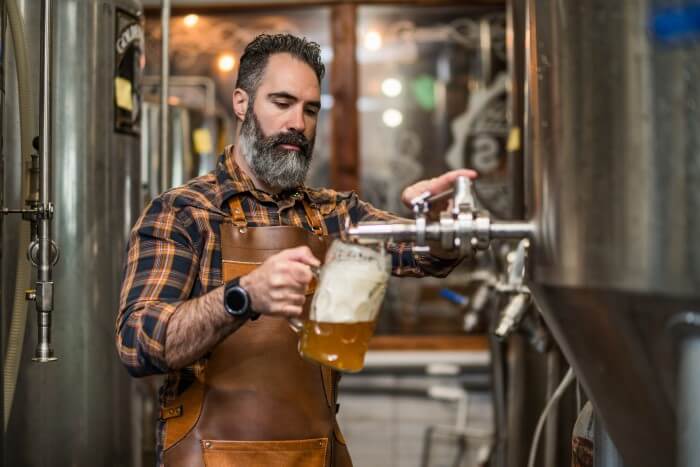 homem servindo um copo de cerveja sem álcool diretamente do tanque de inox