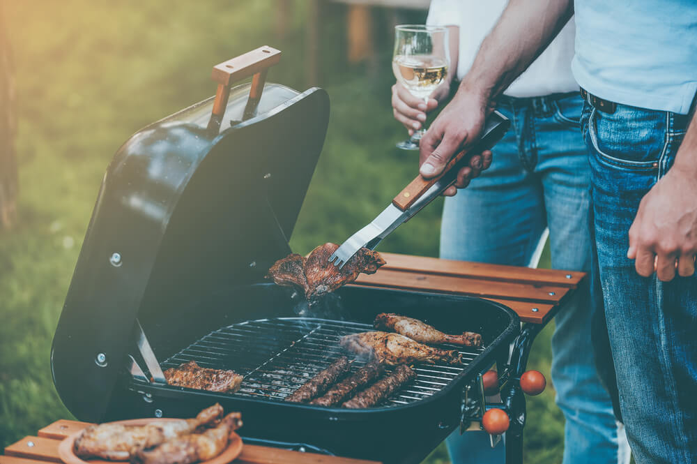 Imagem De Um Homem Fazendo Um Churrasco. Na Imagem, Ele Está Segurando Uma Taça De Vinho.