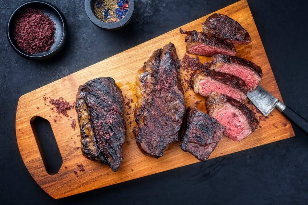 Imagem de uma picanha fatiada em cima de uma tábua de madeira.