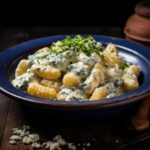 Nhoque de mandioquinha ao molho de gorgonzola dentro de um prato em cima da mesa