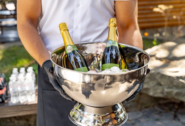 Um homem com luvas segurando um balde com gelos e duas garrafas de bebidas.