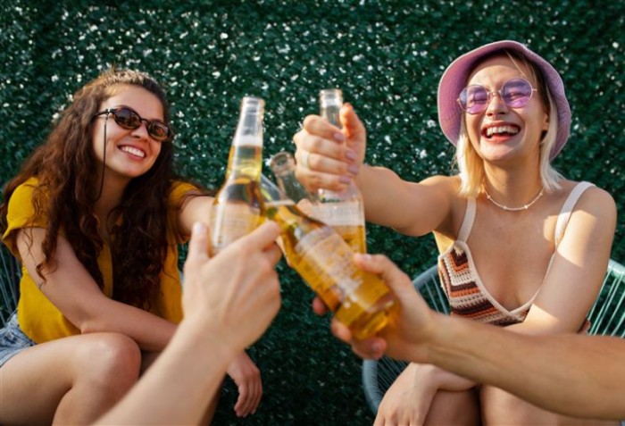 Duas mulheres sorrindo e brindando com outras duas pessoas que só aparecem as mãos