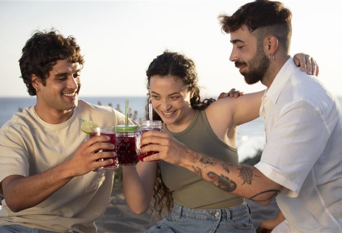 Três pessoas brindando e sorrindo em um local aberto