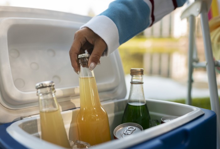 A mão de uma pessoa tocando em uma bebida que está dentro de um cooler com outras bebidas