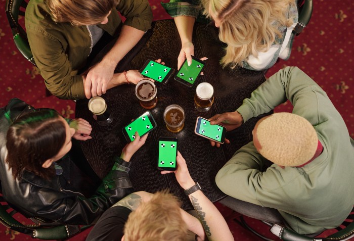 Cinco pessoas sentadas e com os celulares nas mãos jogando o mesmo jogo