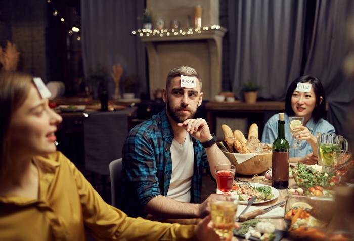 Três pessoas se olhando com papeis nas testas em um jantar