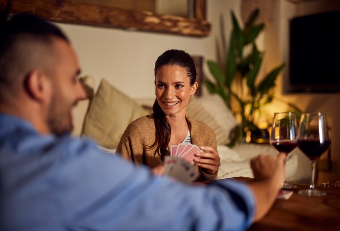 Uma mulher e homem brincando com cartas e taças de vinho sobre uma mesa