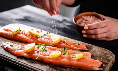 Mãos De Uma Pessoa Temperando Dois Pedaços De Peixes