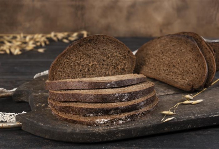 Pães escuros fatiados com um pote de trigo ao lado