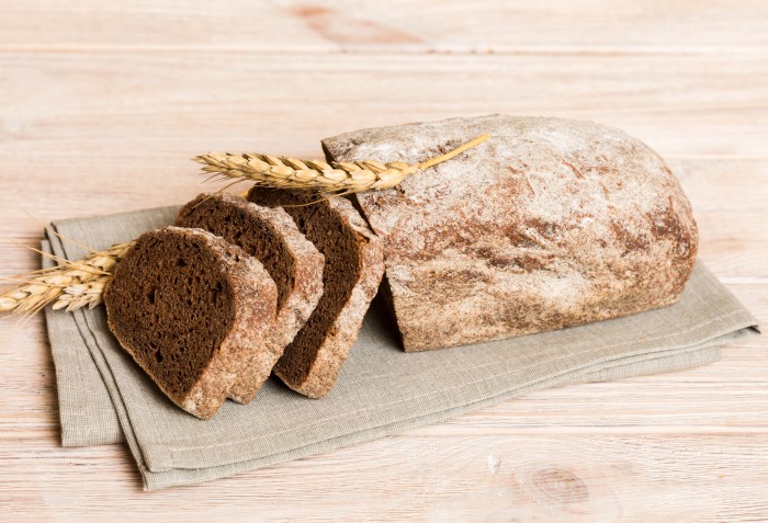Um pão escuro com farinha de trigo em cima e com 3 fatias cortadas ao lado