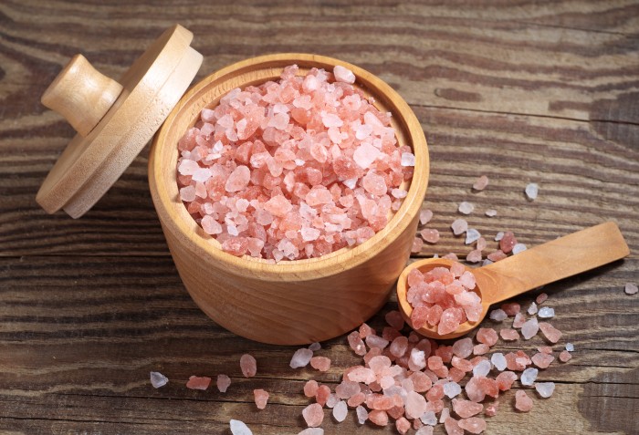 Sal rosa dentro de um pote e despejado ao lado, com uma colher e tampa.