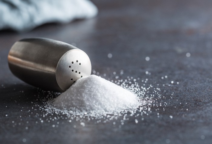 Sal branco despejado fora de um pote de sal prateado.