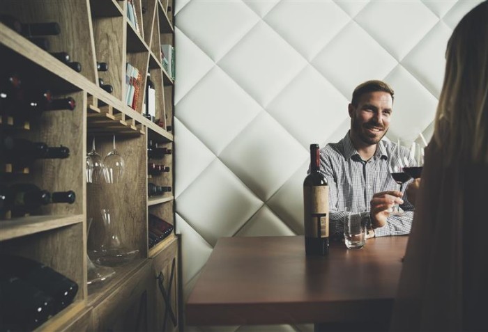 Um casal sentados brindando com vinho em uma adega.