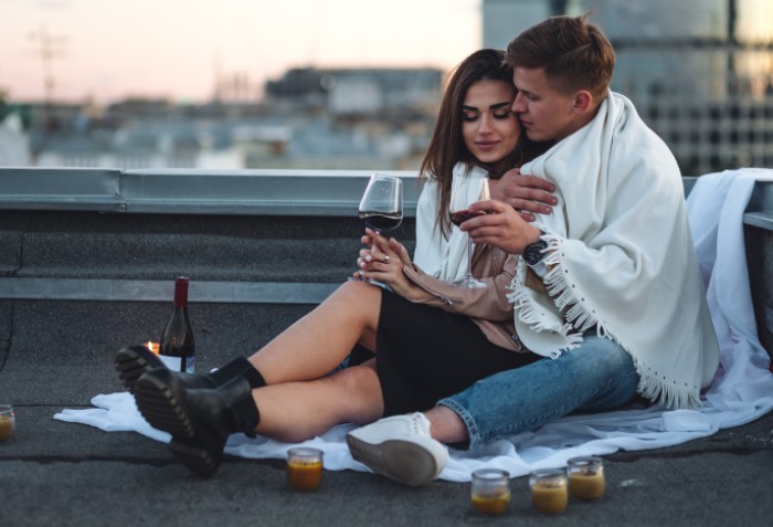 Casal sentados no chão se abraçando e com taças de vinho nas mãos.