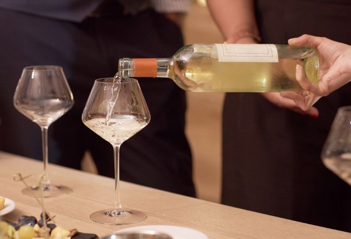 Vinho branco sendo servido para pessoas degustarem.