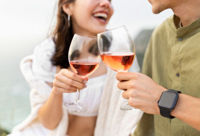 Casal brindando com taças de vinho rosé.